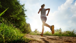 Frau läuft auf einem Feldweg.