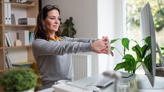 Frau im Homeoffice streckt sich vor Laptop. 