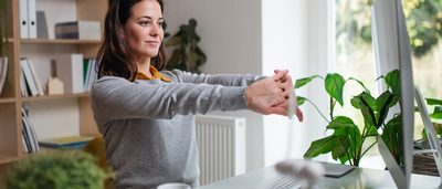 Frau im Homeoffice streckt sich vor Laptop. 