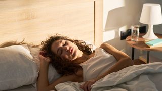 Müde Frau liegt morgens im Bett, während Tageslicht ins Schlafzimmer fällt.