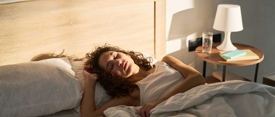 Müde Frau liegt morgens im Bett, während Tageslicht ins Schlafzimmer fällt.