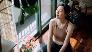 Frau entspannt sitzend im Sonnenlicht mit Pflanzen – Symbol für natürliche PMS-Linderung