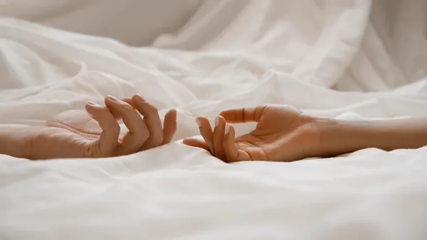 Zwei Hände liegen nebeneinander auf einer weißen Bettdecke.