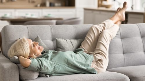 Frau liegt auf einer Couch und legt die Beine hoch.