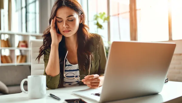Frau sitzt an einen Schreibtisch und fasst sich gestresst an die Schläfe.