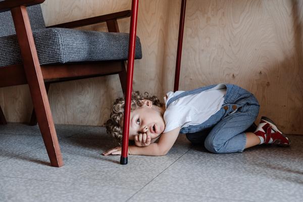 Kleiner Junge liegt unter dem Tisch und reibt sich die Augen