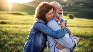 Paar spaziert lachend auf einer Wiese – Symbol für Bewegung in der Natur und Entlastung bei Hämorrhoiden-Beschwerden.