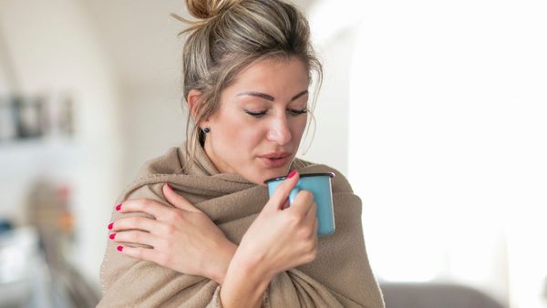Frau mit einer warmen Decke und Tee - Zur Linderung von Erkältungsbeschwerden.