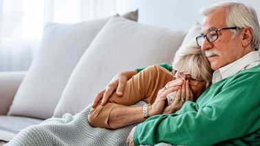 Älteres Paar auf dem Sofa – Frau erkältet mit Taschentuch