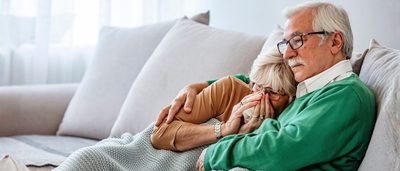 Älteres Paar auf dem Sofa – Frau erkältet mit Taschentuch
