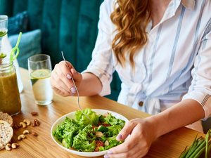 Frau isst eine grüne Salatschüssel mit Gemüse und Nüssen –Mahlzeit im Essensfenster beim Intervallfasten.