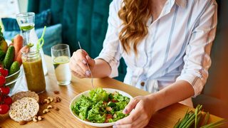 Frau isst eine grüne Salatschüssel mit Gemüse und Nüssen –Mahlzeit im Essensfenster beim Intervallfasten.