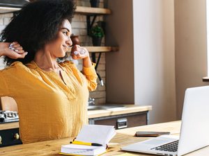 Eine Frau im Homeoffice streckt sich vor dem Laptop – kurze Dehnpause zur Entlastung bei Spannungskopfschmerzen.