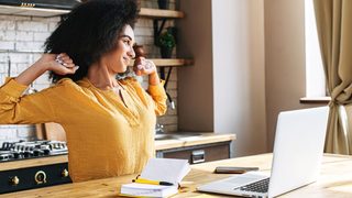 Eine Frau im Homeoffice streckt sich vor dem Laptop – kurze Dehnpause zur Entlastung bei Spannungskopfschmerzen.