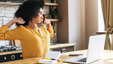 Eine Frau im Homeoffice streckt sich vor dem Laptop – kurze Dehnpause zur Entlastung bei Spannungskopfschmerzen.