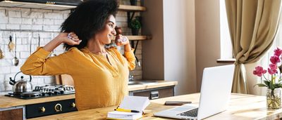 Eine Frau im Homeoffice streckt sich vor dem Laptop – kurze Dehnpause zur Entlastung bei Spannungskopfschmerzen.