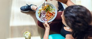 Person sitzt auf der Matte und isst eine bunte Gemüse-Bowl mit Hülsenfrüchten; zuckerarme Mahlzeit unterstützt Lebergesundheit und Insulinsensitivität.
