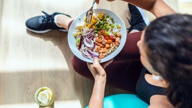 Person sitzt auf der Matte und isst eine bunte Gemüse-Bowl mit Hülsenfrüchten; zuckerarme Mahlzeit unterstützt Lebergesundheit und Insulinsensitivität.