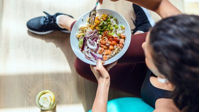 Person sitzt auf der Matte und isst eine bunte Gemüse-Bowl mit Hülsenfrüchten; zuckerarme Mahlzeit unterstützt Lebergesundheit und Insulinsensitivität.