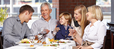 Mehrgenerationen-Familie beim Essen mit Wasser und Salat; Symbol für ausgewogene Ernährung, Leber entgiften und Darmgesundheit.