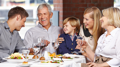 Mehrgenerationen-Familie beim Essen mit Wasser und Salat; Symbol für ausgewogene Ernährung, Leber entgiften und Darmgesundheit.
