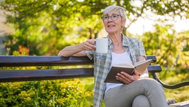 Ältere Frau liest im Garten – Informationen zur Blasenentleerungsstörung im Alter
