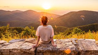 Person sitzt bei Sonnenuntergang auf einer Steinmauer– Symbol für Sonnenlicht und Vitamin D für Gelenke und Knochen.