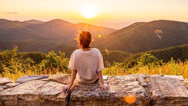 Person sitzt bei Sonnenuntergang auf einer Steinmauer– Symbol für Sonnenlicht und Vitamin D für Gelenke und Knochen.