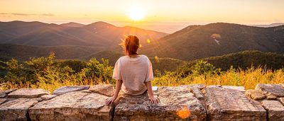 Person sitzt bei Sonnenuntergang auf einer Steinmauer– Symbol für Sonnenlicht und Vitamin D für Gelenke und Knochen.