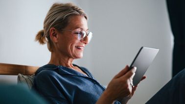 Person sitzt entspannt im Schlafzimmer und bedient Smart-Home-Funktionen über ein Tablet