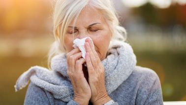 Ältere Frau mit Schal putzt sich die Nase
