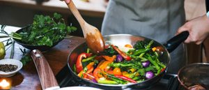 Person rührt eine bunte Gemüsepfanne mit Brokkoli, Paprika und Bohnen –Ernährung bei Rheuma.