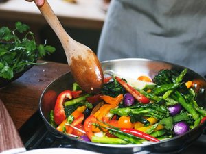 Person rührt eine bunte Gemüsepfanne mit Brokkoli, Paprika und Bohnen –Ernährung bei Rheuma.