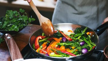 Person rührt eine bunte Gemüsepfanne mit Brokkoli, Paprika und Bohnen –Ernährung bei Rheuma.