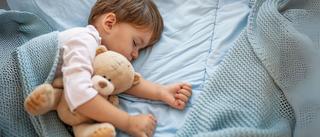 Kleiner Junge schläft mit Teddybär im Bett