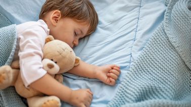 Kleiner Junge schläft mit Teddybär im Bett
