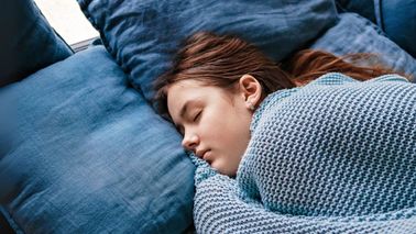 Schlafende Jugendliche unter blauer Strickdecke auf dem Sofa.