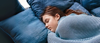 Schlafende Jugendliche unter blauer Strickdecke auf dem Sofa.