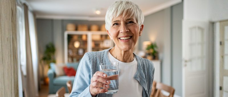 Fröhliche und vitale ältere Frau hält ein Glas Wasser in der Hand - Symbol für gesundes Altern