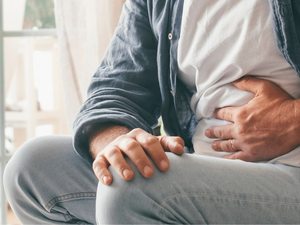 Mann mit Bauchkrämpfen hält sich den Bauch auf dem Sofa