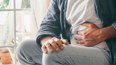 Mann mit Bauchkrämpfen hält sich den Bauch auf dem Sofa