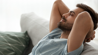 Ein Mann lehnt sich entspannt auf dem Sofa zurück - Symbol für Resilienz