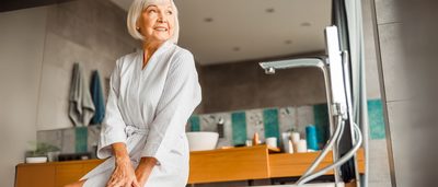Ältere Frau sitzt lächelnd am Badewannenrand – sie wirkt sicher in ihrem modernen Badezimmer.