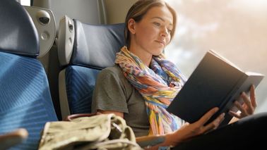 Frau sitzt entspannt im Zug und liest ein Buch, um unterwegs zu entspannen.