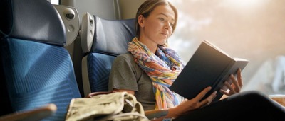 Frau sitzt entspannt im Zug und liest ein Buch, um unterwegs zu entspannen.