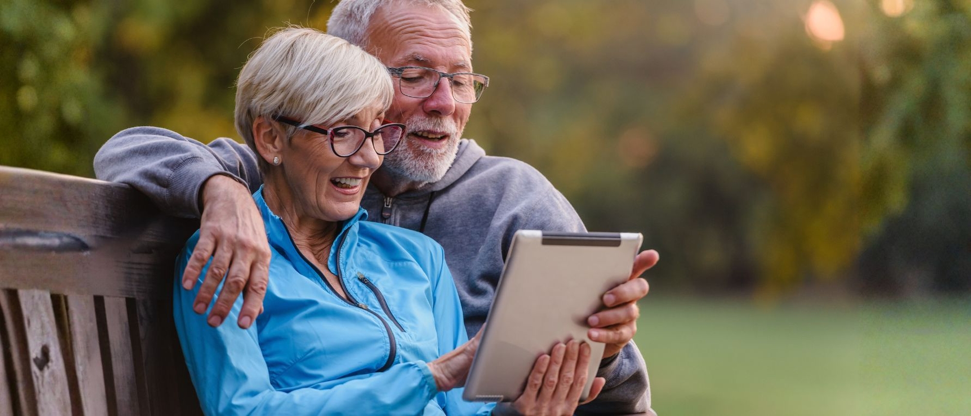 Älteres Paar sitzt zufrieden auf einer Parkbank und informiert sich über Longevity