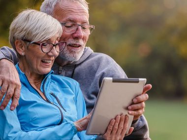 Älteres Paar sitzt zufrieden auf einer Parkbank und informiert sich über Longevity