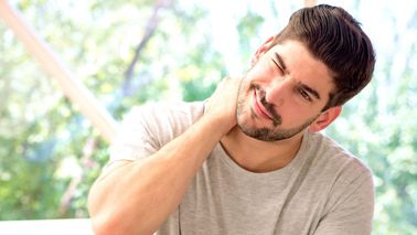 Mann fasst sich an den Nacken – typische Nackenschmerzen morgens durch Verspannungen