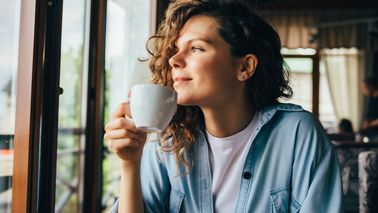 Frau sitzt am Fenster und trinkt eine Tasse Kaffee