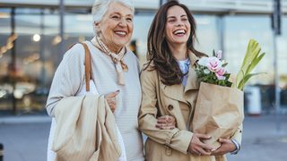 Zwei Frauen lachen und tragen Einkaufstaschen beim gemeinsamen Stadtbummel.